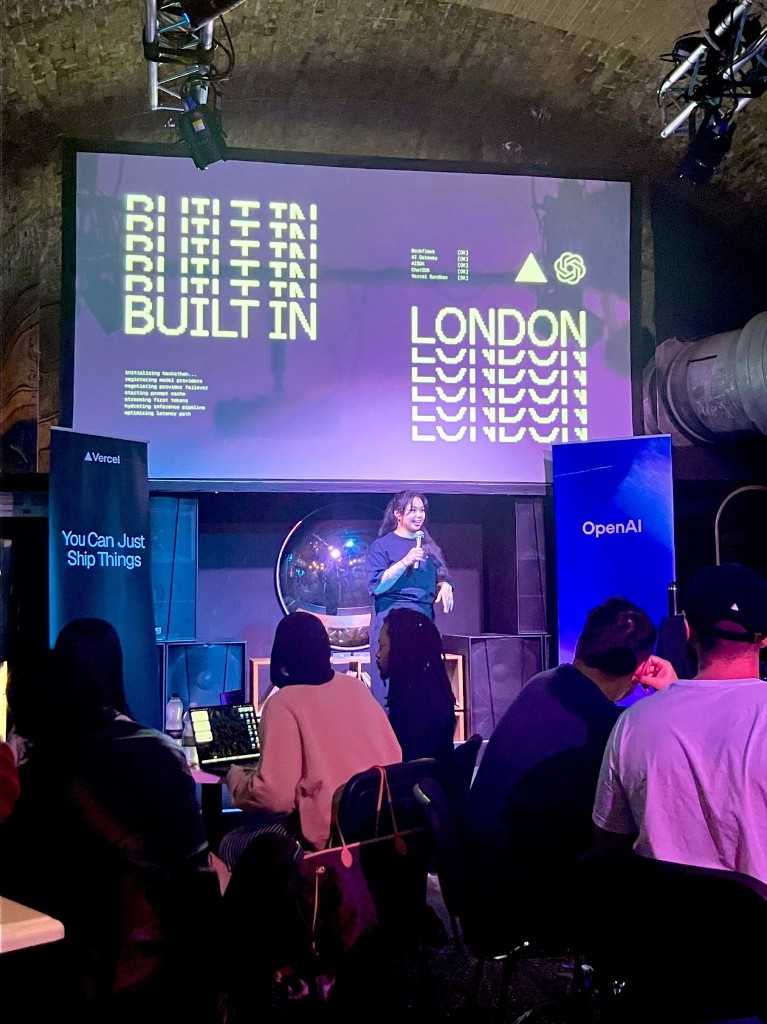 Maya on stage at Built in London presenting in front of the Built in London screen