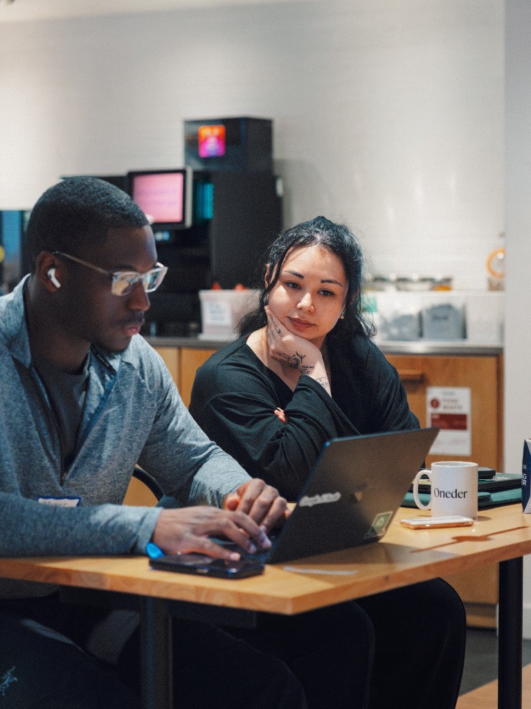 Supporting a developer at a community hackathon, working together at a table with a laptop