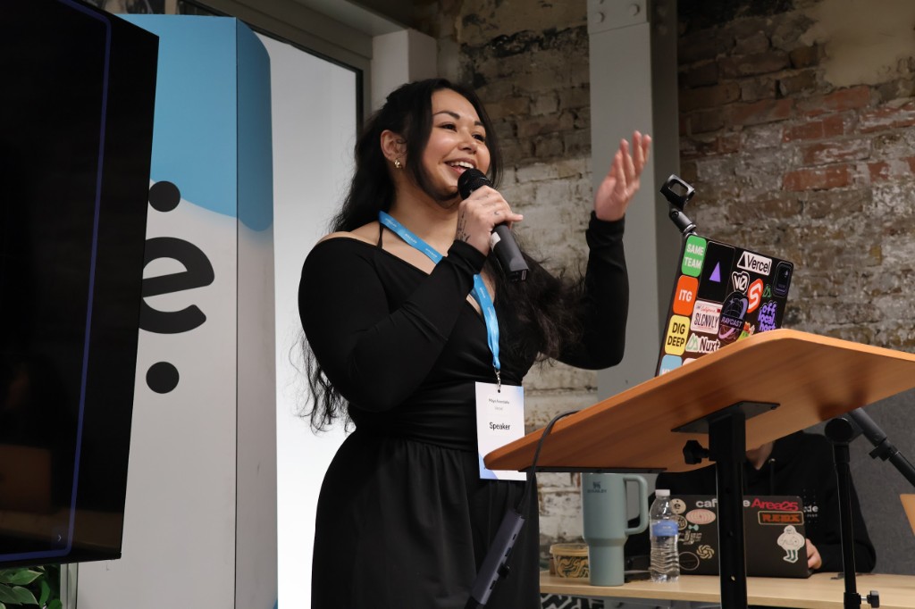 Maya speaking at Encode AI London 2026, Speaker badge, laptop with Vercel stickers